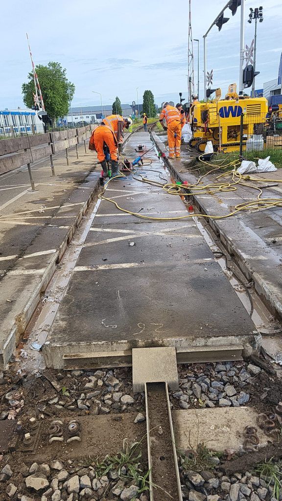 Medewerkers van De Wilde Spoorwegbouw boren de ankerhulzen uit in de raildraagplaten van de overweg
