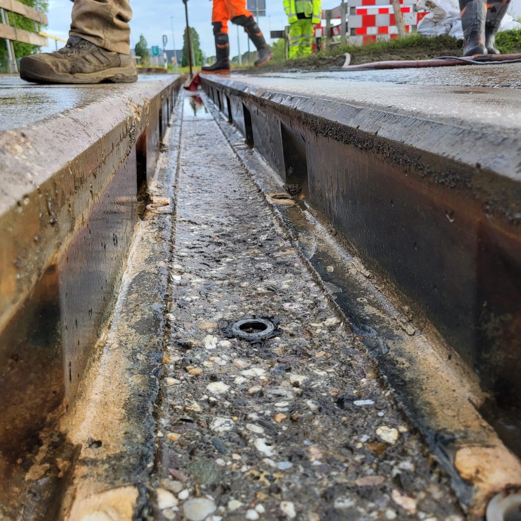 Uitgefreesde spoorgoot in de overweg, met de ankerhulzen in de raildraagplaat zichtbaar
